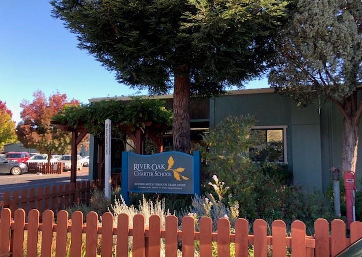 River Oak Charter School front of school with brown fence and blue River Oak sign.